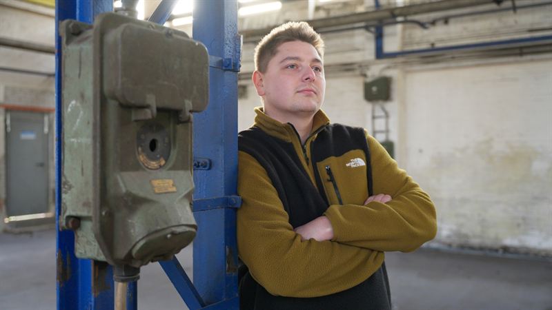 Ein junger Mann mit verschränkten Armen lehnt an einer alten Industriesäule mit Schaltkasten, ernster Blick in die Ferne – Szene aus der EB-Produktion 'Funk – Der Dunkle Parabelritter'