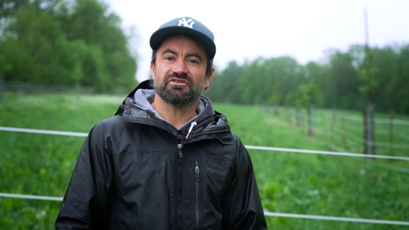 Ein Mann mit Cap steht auf einer grünen Weide und spricht in die Kamera – Szene aus der Imagefilmproduktion für Pulsschlag Erde e.V.