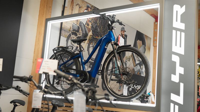 Beleuchtete Werbetafel mit E-Bike im Zweiradhaus Lorenz, im Hintergrund ein Mitarbeiter – Werbefilm für Zweiradhaus Lorenz